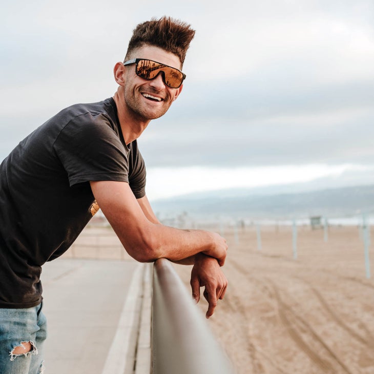 Eamon Lucas wearing sunglasses and leaning on a rail overlooking a beach