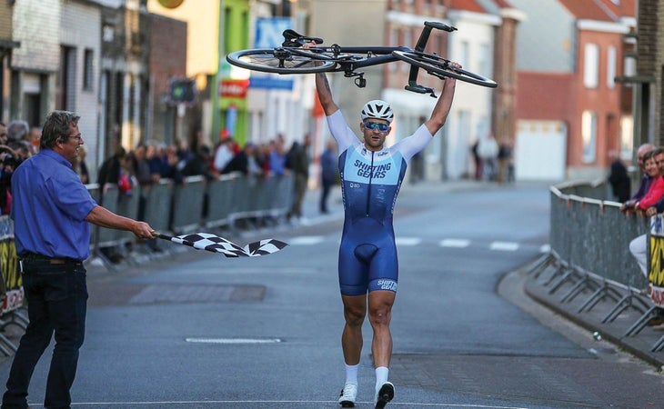 A race official waves a checkered flag as Eamon Lucas crosses the finish line with his bike held high overhead