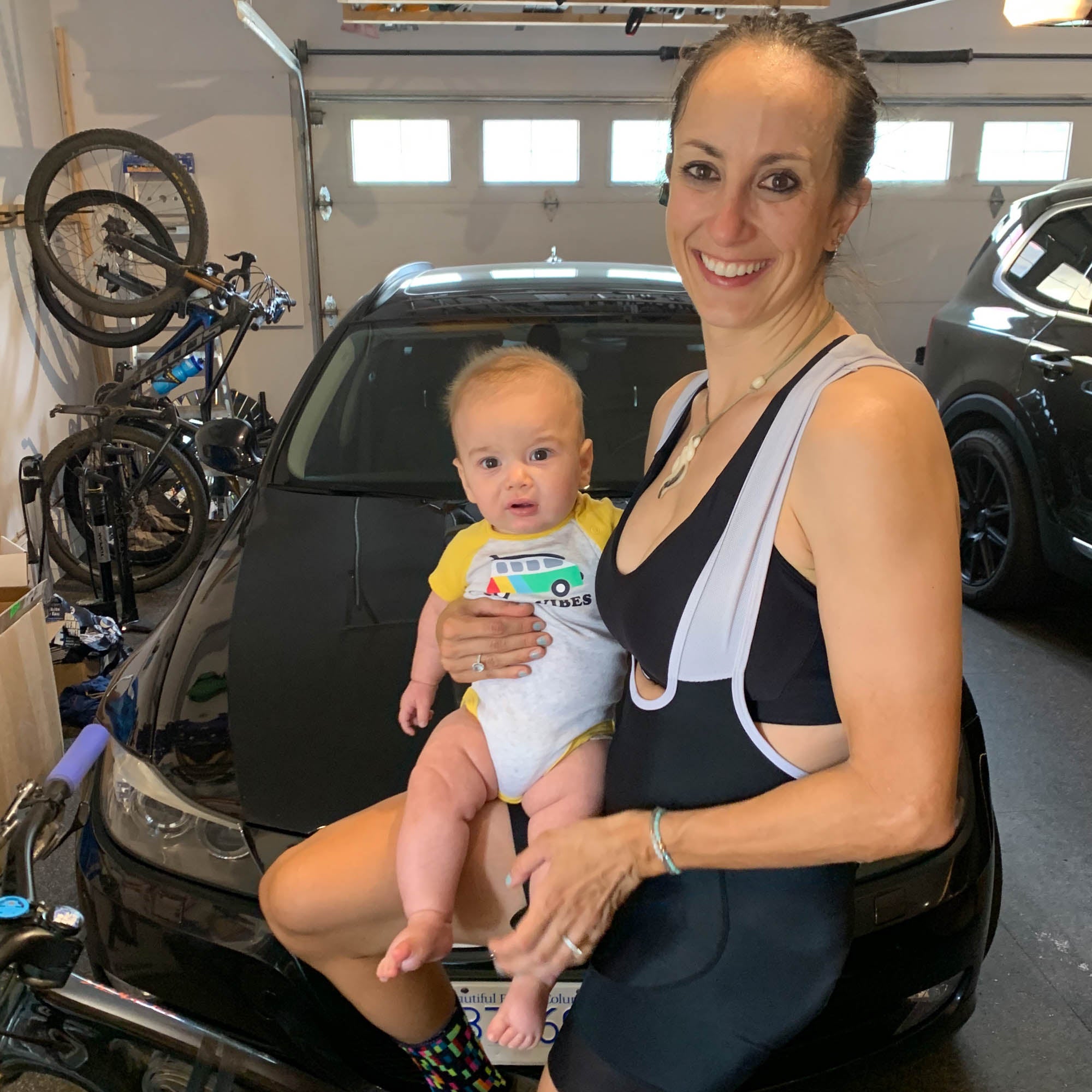 Sonya holds her son while sitting on an indoor trainer in the garage