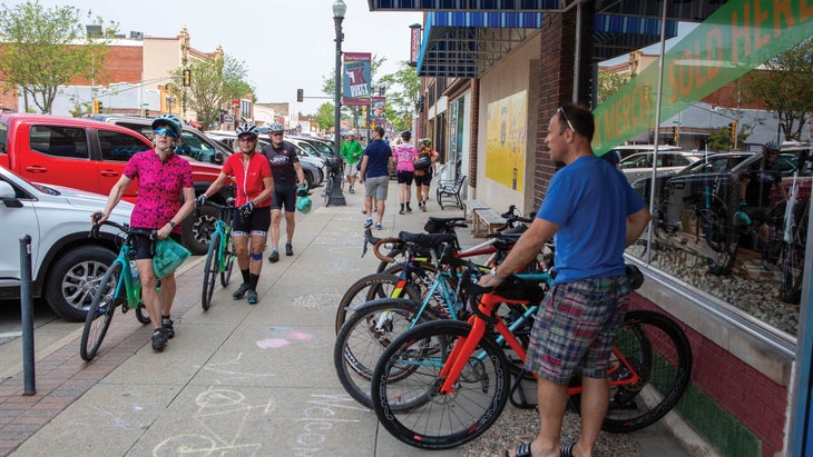 Cyclists line up their bikes outside a storefront in a small downtown area