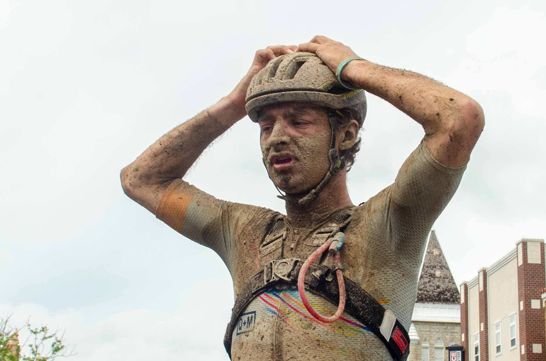 A mud covered gravel cyclist Alexey Vermeulen holds his hands to his head after finishing Unbound Gravel 2022