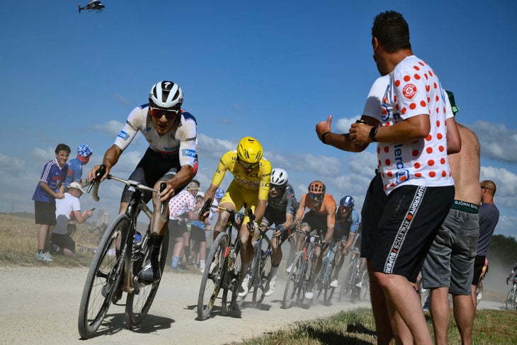 Soudal Quick-Step team's Belgian rider Remco Evenepoel wearing the best young rider's white jersey (L) followed by UAE Team Emirates team's Slovenian rider Tadej Pogacar wearing the overall leader's yellow jersey cycle with the pack of riders (peloton) over a "Chemin Blanc" (white road) gravel sector during the 9th stage of the 111th edition of the Tour de France cycling race, 199km stage departing and finishing in Troyes, on July 7, 2024. (Photo by Marco BERTORELLO / AFP)