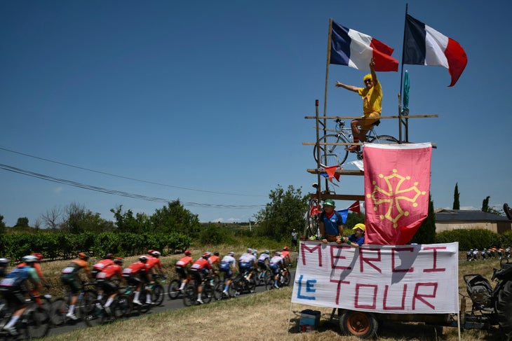 Concerns for French Cycling on Eve of Tour de France Reveal 3 The pack of riders (peloton) cycles past a spectator atop a makeshift tower adorned with a banner which reads "Thank you, Tour" and French national and Occitan regional flags during the 16th stage of the 111th edition of the Tour de France cycling race, 188,6 km between Gruissan and Nimes, southern France, on July 16, 2024. (Photo by Marco BERTORELLO / AFP)