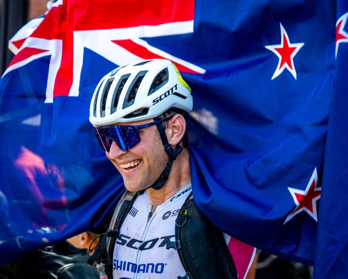 Cameron Jones issa una bandiera della Nuova Zelanda sopra la sua testa dopo la gara di mountain bike Little Sugar.