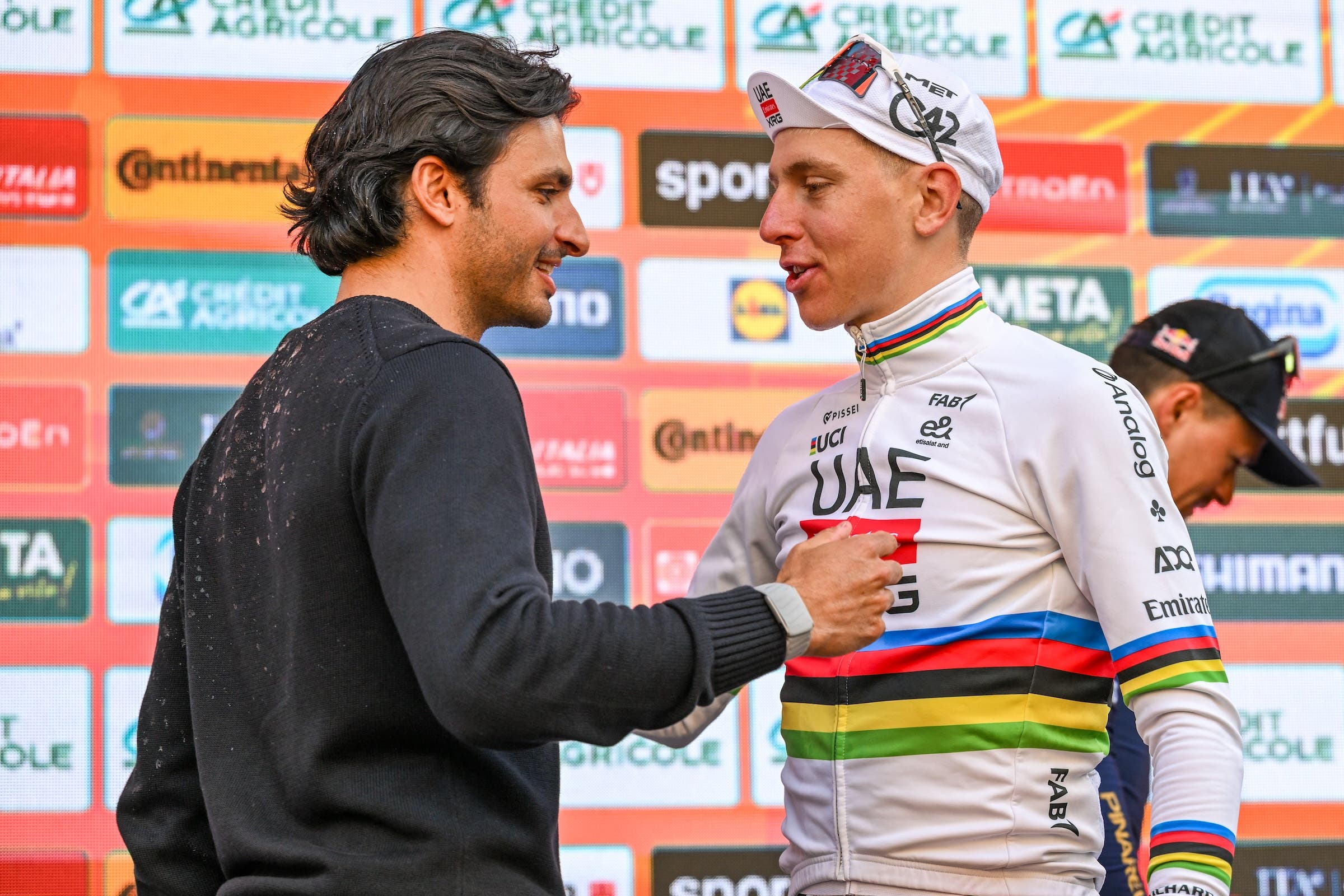 Il pilota Carlos Sainz e il vincitore della gara Tadej Pogacar (UAE Emirates-XRG) sul podio dopo la Milano-San Remo (Foto: David Pintens/Belga Mag via AFP)