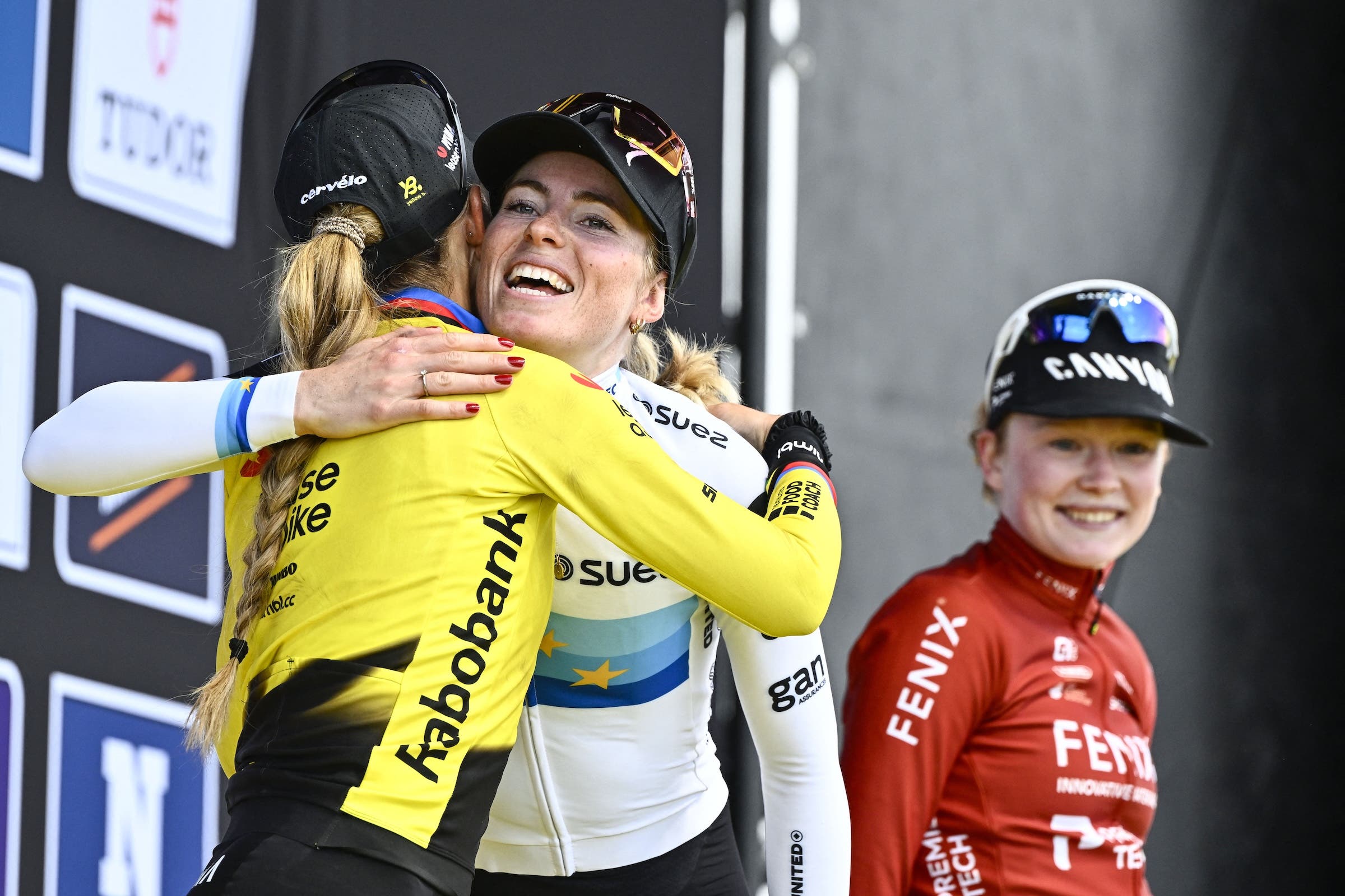 Demi Vollering hugs runner-up Pauline Ferrand-Prévot on the podium of the Tour of Flanders while Puck Pieterse smiles (Photo: Eric Lalmand / Belga mag via AFP)